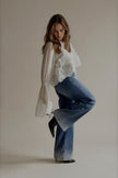Blouse CAPUCINE blanche à broderies portée avec un jean bleu à strass