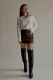 Jupe-short JOYCE marron effet cuir portée avec une chemise blanche, silhouette entière