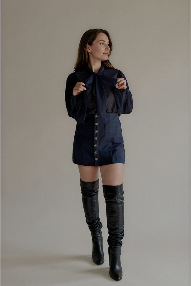 Jupe JOY courte bleu marine à boutons décoratifs portée avec une chemise lavallière

