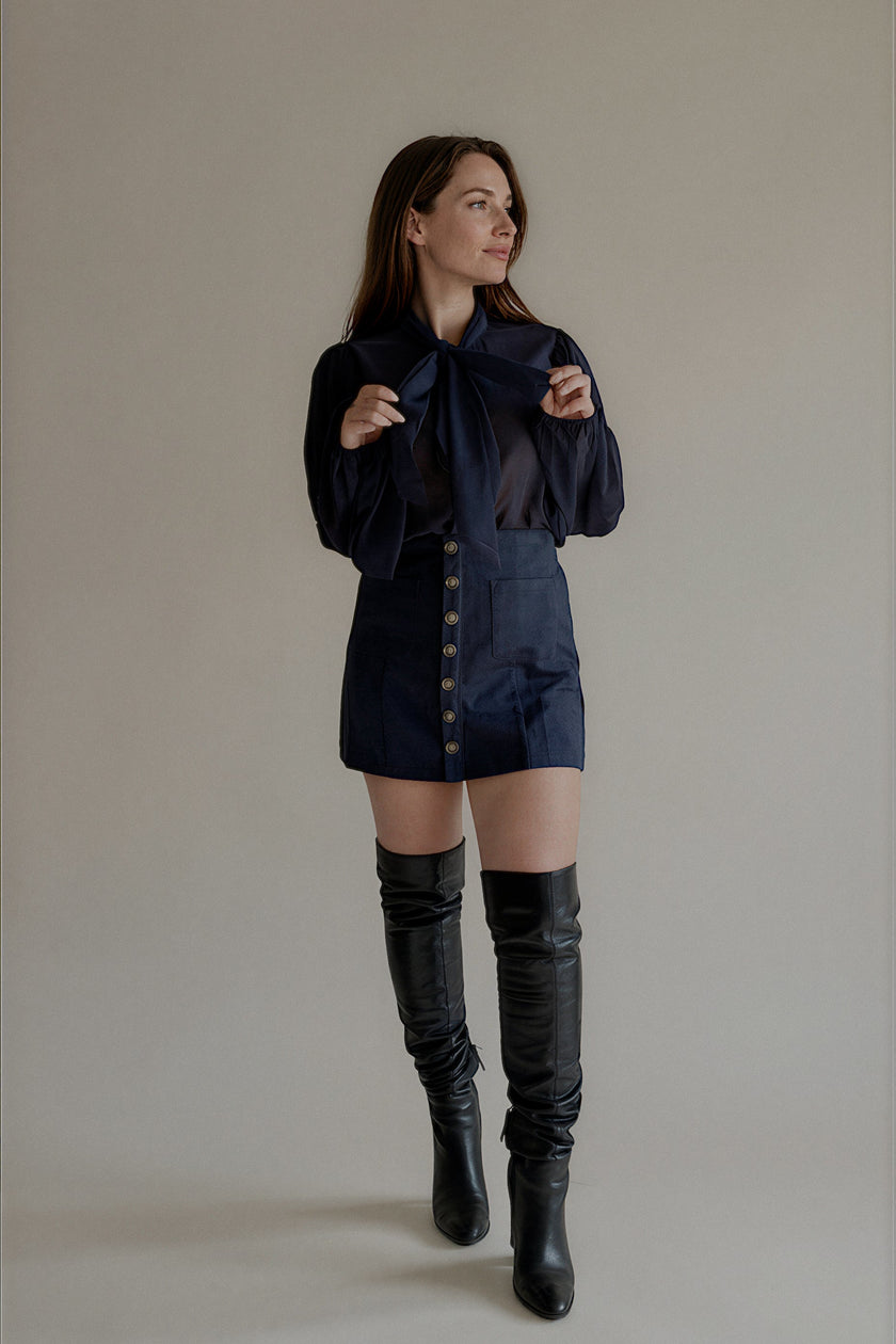Jupe JOY courte bleu marine à boutons décoratifs portée avec une chemise lavallière

