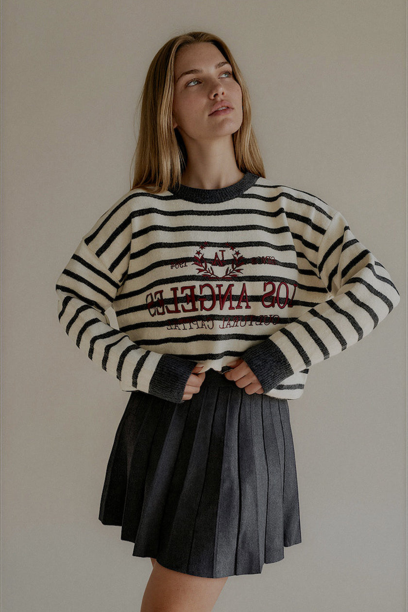 Pull MONROE rayé écru et gris avec inscription bordeaux, porté avec une jupe plissée