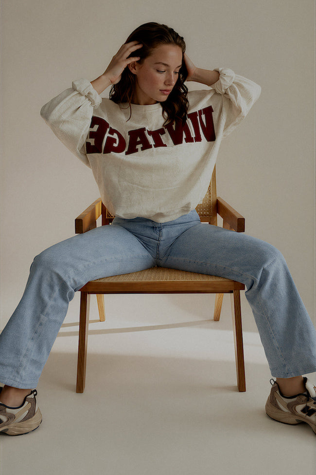 Sweat SIXTINE gris chiné à inscription bordeaux porté assis avec un jean clair