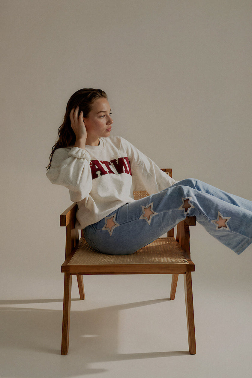Sweat SIXTINE gris chiné à inscription bordeaux porté assis avec un jean clair