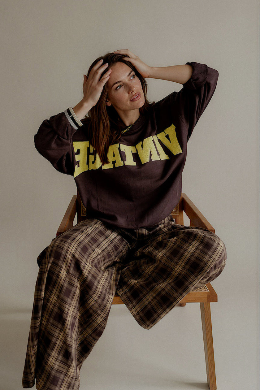 Sweat SIXTINE marron et jaune porté assis avec un pantalon à carreaux