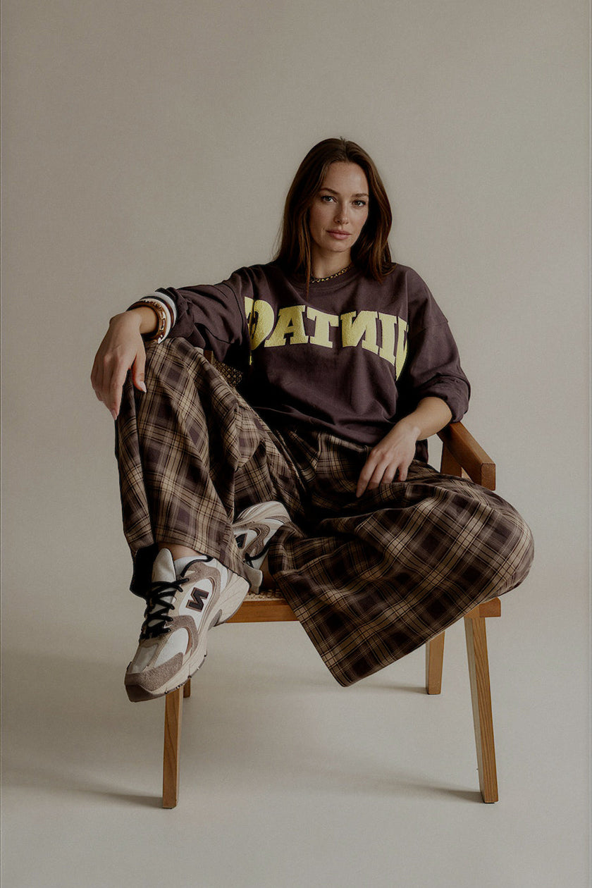 Sweat SIXTINE marron à inscription jaune porté avec un pantalon large à carreaux
