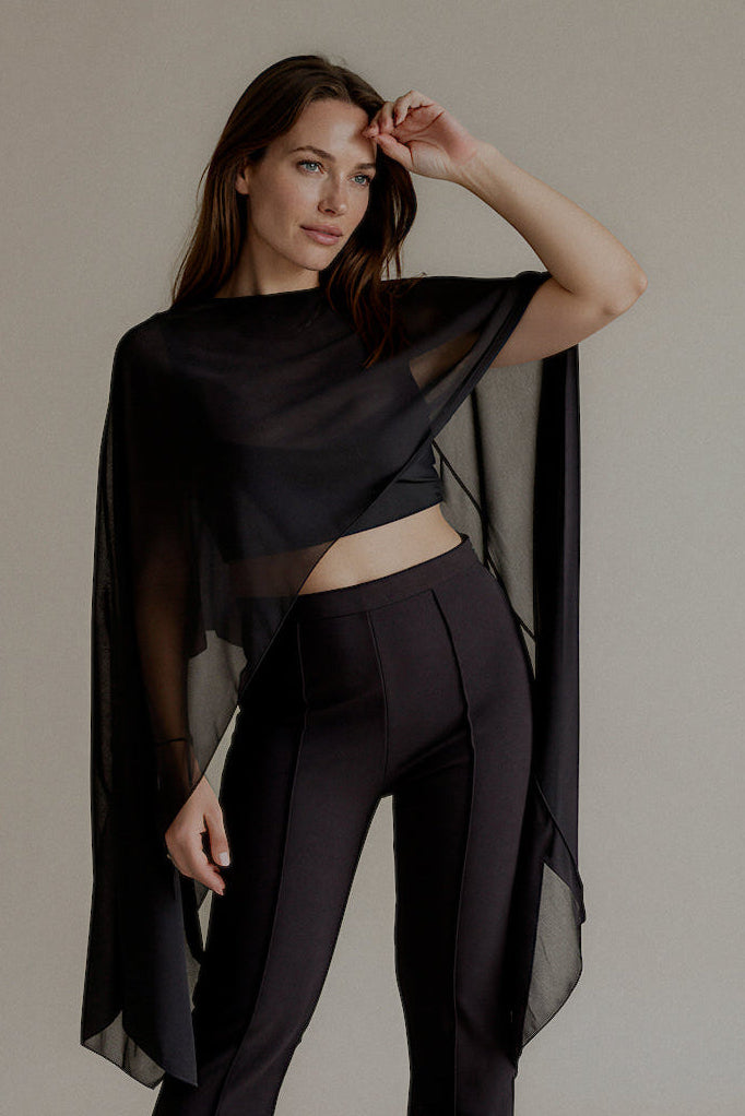 Top THÉA noir transparent à la coupe asymétrique porté avec un pantalon noir