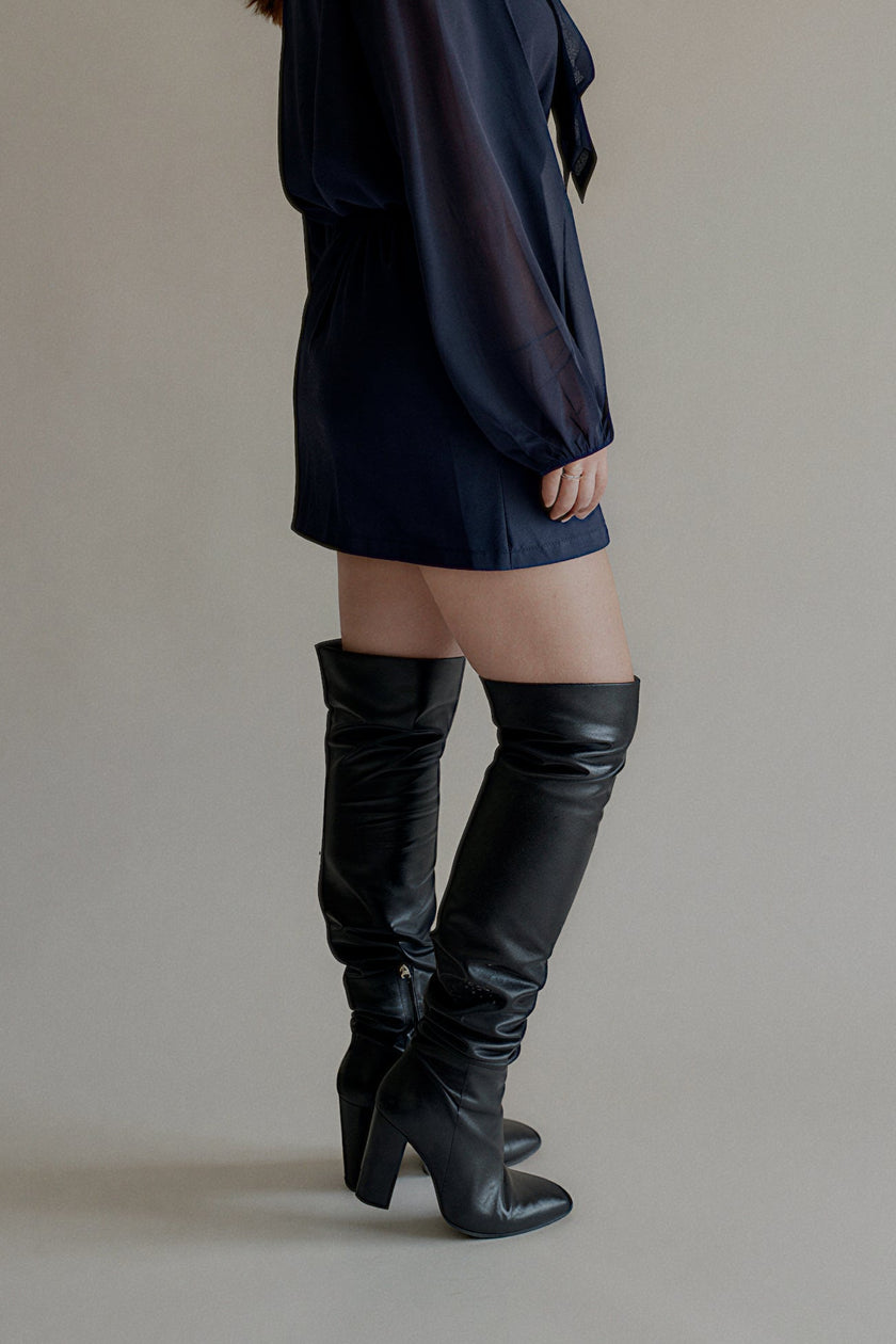 Vue de profil de la jupe JOY courte bleu marine portée avec des bottes hautes