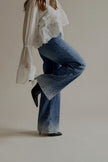 Vue de profil du jean PAIGE bleu à strass porté avec une blouse blanche